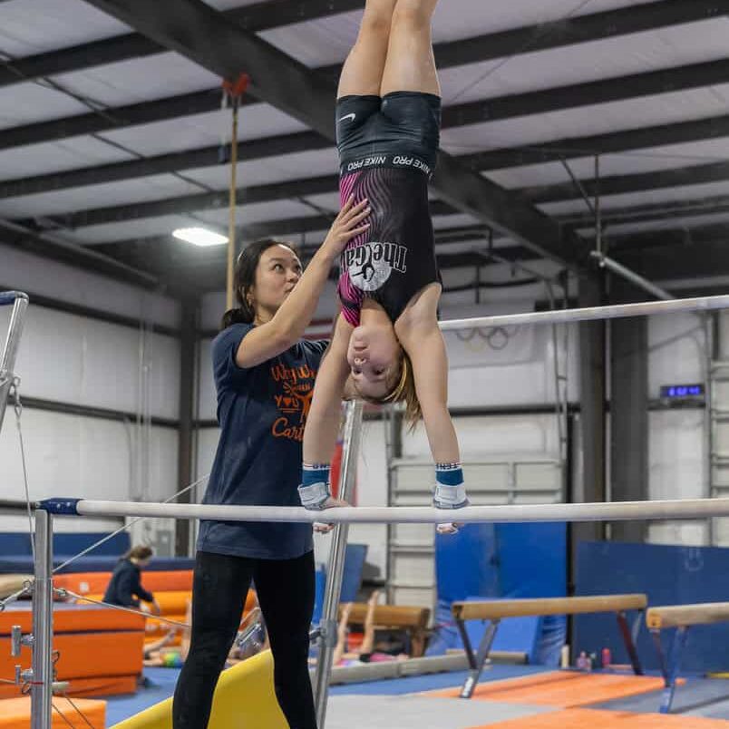 Joy Mays assisting a gymnast on bars